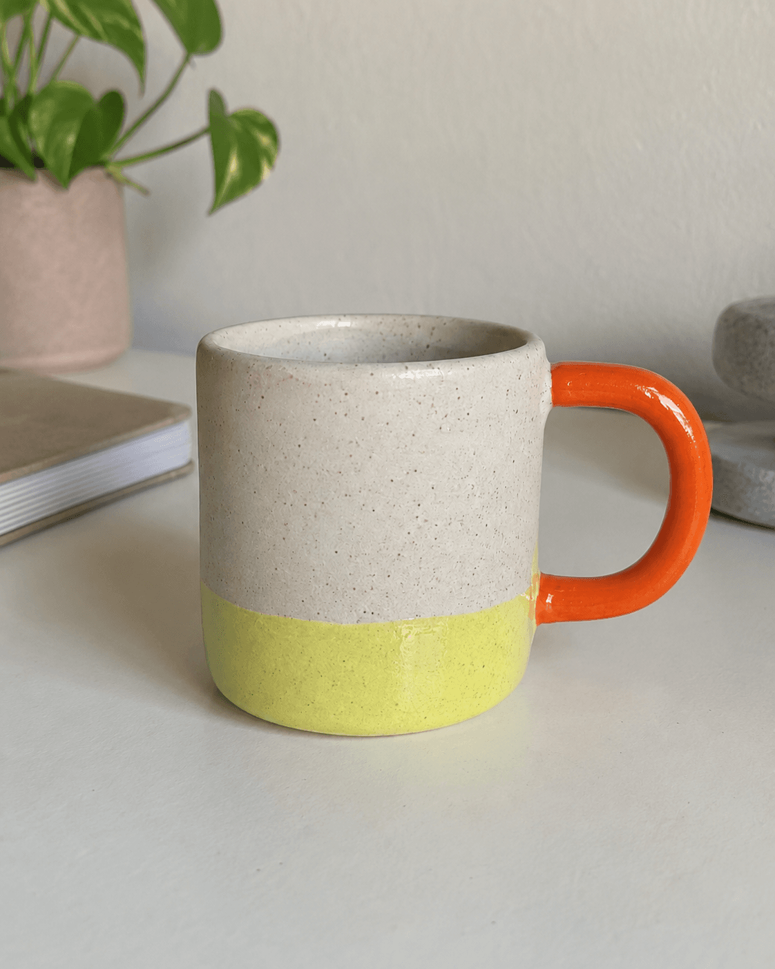 Original photo of a handmade speckled ceramic mug with a citron glaze dip and orange handle