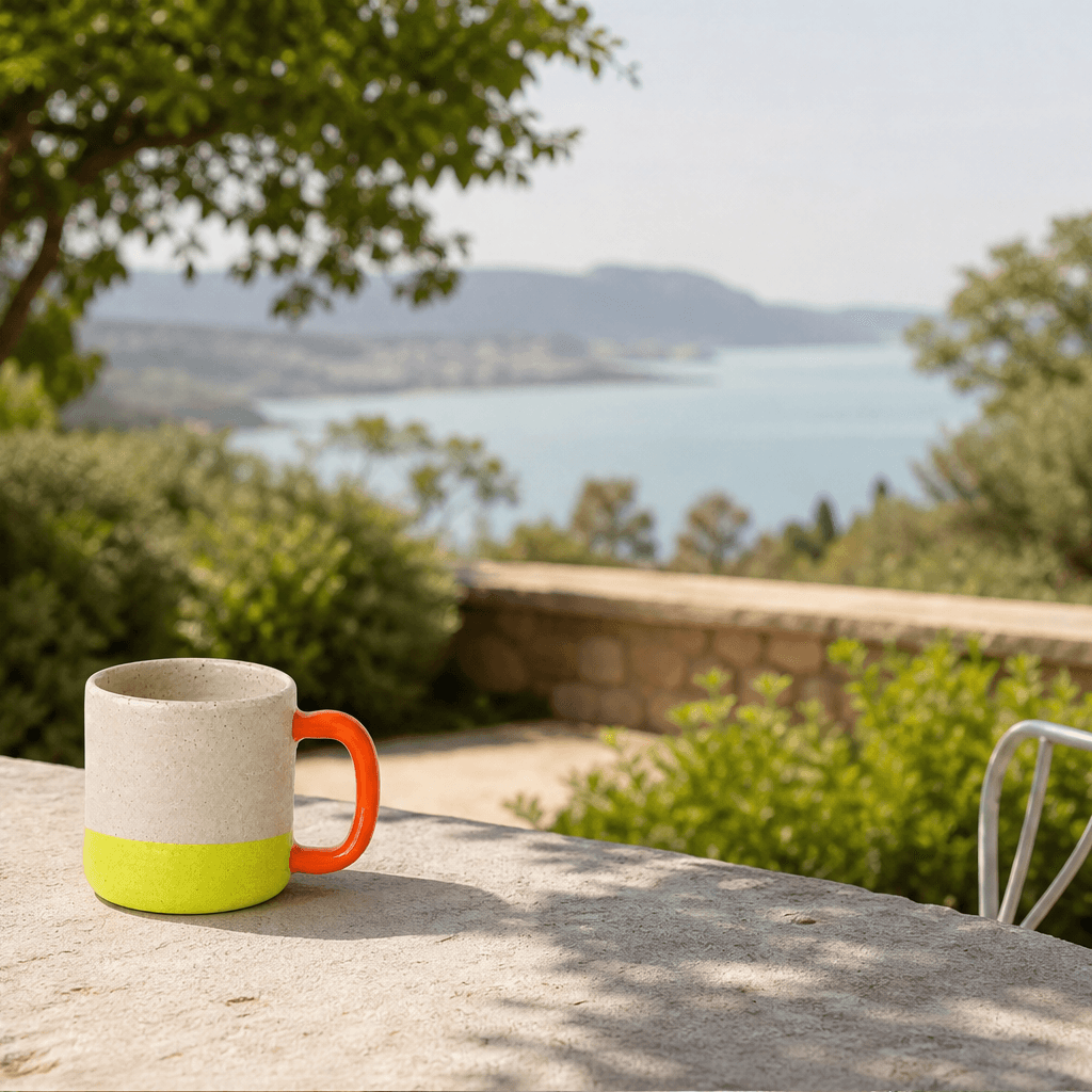 The same handmade ceramic mug on a sunlit terrace overlooking the coast
